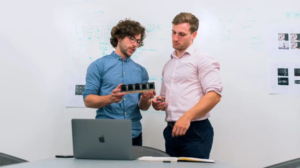 Equipo de emprendedores tecnológicos revisando un prototipo en una oficina, relacionado con iniciativas de empleo de base tecnológica.